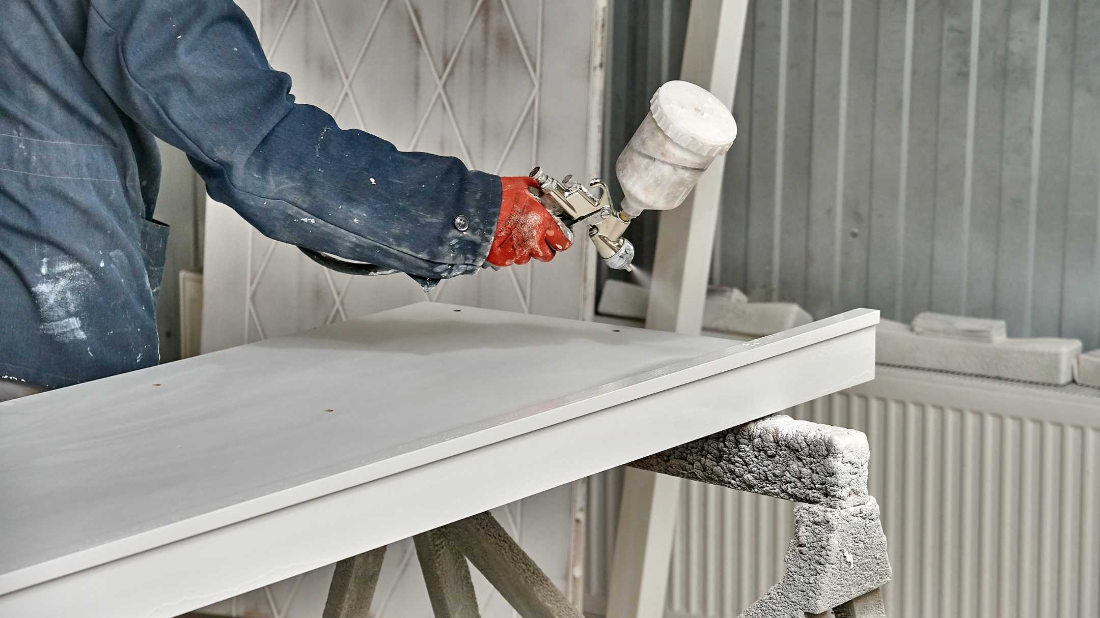 professional in blue painter's uniform spray painting white cabinets