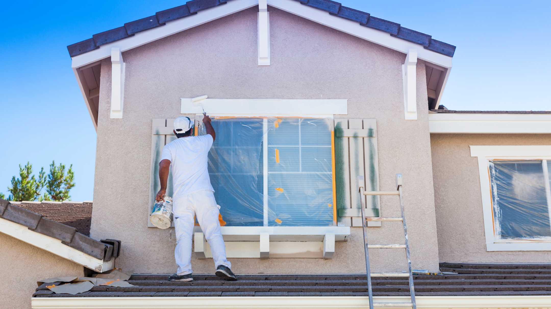 professional in white uniform painting exterior of home